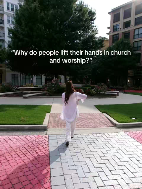 A woman walks away from the viewer. The background includes buildings and lots of green trees.