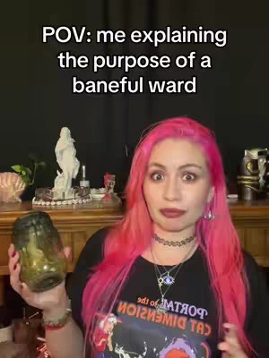 A woman with bright pink hair stands in front of a dark background, holding a glass jar and looking toward the camera. Text overlays read, 'POV: me explaining the purpose of a baneful ward.' The woman is dressed in a black T-shirt.