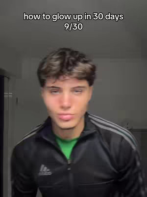 The cover image features a young man, centered and facing the viewer, against a gray or neutral background that suggests an indoor setting. The man has short, textured dark hair. He wears a green shirt beneath a black Adidas jacket with white stripes. The text overlayed on the top of the image reads, 'how to glow up in 30 days 9/30'. He has a slightly upward gaze and a neutral expression, and he is looking directly into the camera.