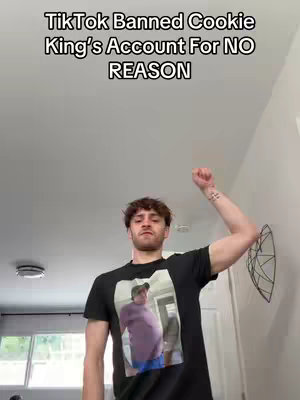 The cover image features a man in a room, with text overlayed at the top. The man is positioned center, wearing a black t-shirt with a printed photo on it, and raising his right arm with fist clenched. Behind him is a white wall, with a decorative object hanging on the side. The lighting is natural, casting soft shadows.