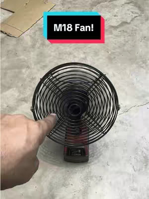 The cover image shows a close-up of a black fan with a round, cage-like guard. The fan is resting on top of a red and black battery pack, likely an M18 model. A hand with a visible index finger points towards the fan, and overlayed text reads "M18 Fan!" in a color block frame. The background appears to be a concrete surface.