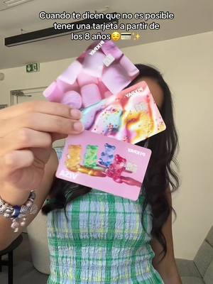 A person holds up three colorful Pixpay cards in front of them. The cards feature playful designs, with the top card showing a pink and purple theme, the middle card with a mix of colors, and the bottom card with gummy bears. Text is overlaid at the top about having a card from 8 years old.