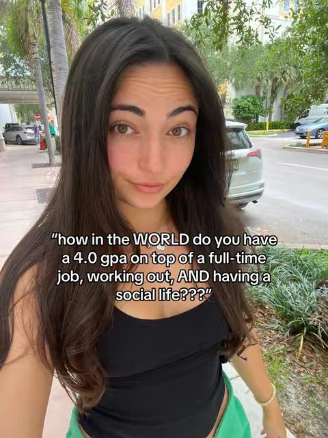 A young woman with long brown hair poses for a selfie in an outdoor setting with green foliage and a building in the background. Text overlayed on the image poses the question, "how in the WORLD do you have a 4.0 GPA on top of a full-time job, working out, AND having a social life???"
