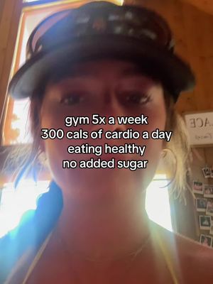 A selfie-style image featuring a person wearing a black cap with sunglasses on it, at eye-level with visible text overlaying the face. The person has visible skin and hair, with a background that suggests a residence or a room with wooden finishes. The framing is close and focuses on the face and upper body.