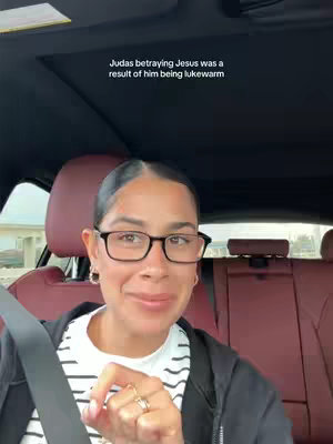 A woman wearing glasses smiles while sitting the front seat of a car. The seat behind her is red, and a sign is visible out the drivers side window. Text appears above her head.