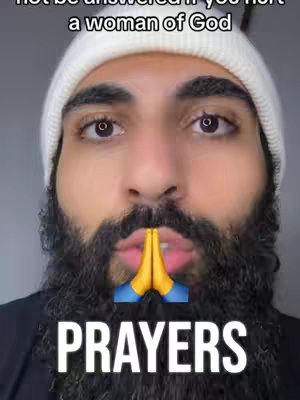 A selfie-style image with a man in a white beanie looking directly at the camera. He has a beard, and his hands are positioned in a prayer gesture with a yellow and blue praying hands emoji positioned in between. Below the hands, the word 'PRAYERS' is written in large white, bold text. Above him, is the text "Not be answered if you hurt a woman of God".