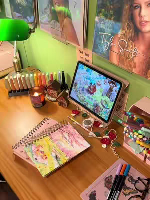 A desk setup with a notebook, an iPad, and other study-related items. The color scheme is primarily pastel pink, green, and gold with the backdrop of album covers.