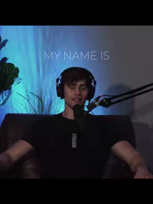 A man wearing headphones and a black t-shirt sits in front of a microphone. The background has blue and white lighting. Text overlaying the image reads "MY NAME IS".