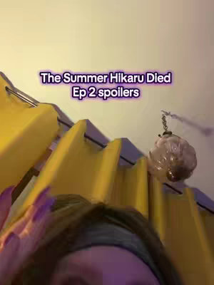 The image is a vertical shot featuring a person's face in the foreground, with their hand visible, possibly reaching toward the top left of the frame. The background is a blurred room with yellow curtains and a decorative hanging object with a chain. Text overlay in the center reads "The Summer Hikaru Died Ep 2 spoilers". The overall composition is centered, using slightly warm lighting.