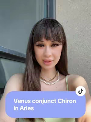 A selfie-style shot featuring a woman with long brown hair and bangs, wearing a layered gold necklace, and a light green spaghetti strap top. She is positioned indoors with a plain background, and a text overlay appears on the lower portion of the screen.