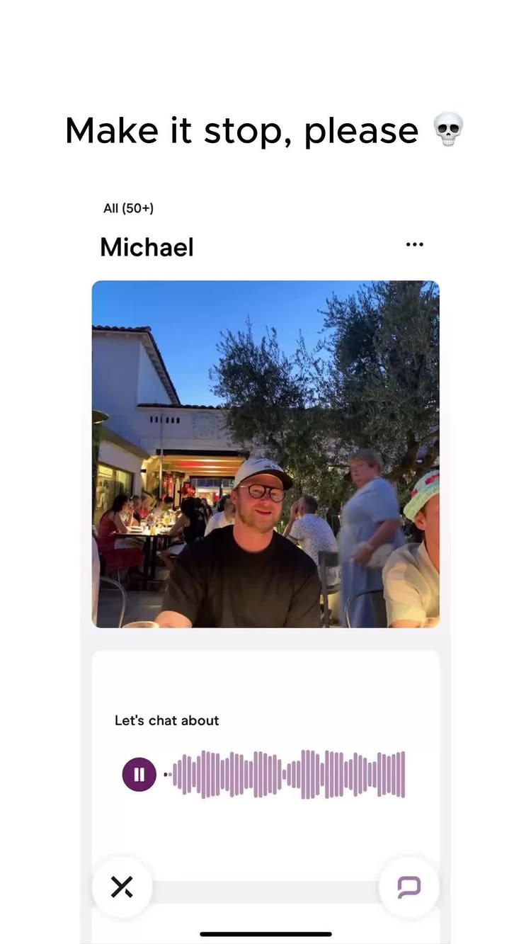 The image is from a dating app.  A man with glasses and a baseball cap is centered in the frame, seated at a table outside a restaurant. The background includes a mix of other individuals and outdoor lights. The app interface shows a message from a person named Michael.
