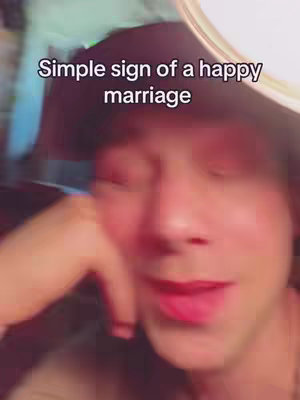 A selfie-style video cover image featuring a person looking directly at the camera with a slightly upturned expression, their mouth is slightly open. On the top it has the text overlayed: Simple sign of a happy marriage.