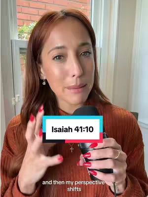 A woman with red hair and red nail polish holds a microphone in front of a window. A text overlay says Isaiah 41:10.