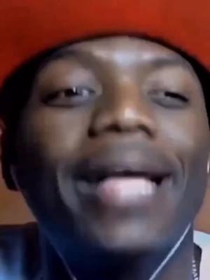 A close-up shot of a young Black man with a red hat, looking directly at the camera with a slight smile and his mouth open as if speaking. The background is blurred, focusing attention on his face. The lighting appears natural, and the composition is simple, highlighting his expression and connection with the viewer.