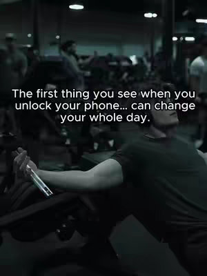 A grayscale image set inside a gym. In the background, other men work out with weights and machines. In the foreground, a man is angled towards the center right, appearing to be resting his forearm on a weight machine while holding a phone in the crook of that arm. Overlay text in the upper part of the frame appears to be a life-affirming motivational quote in a sans-serif font.