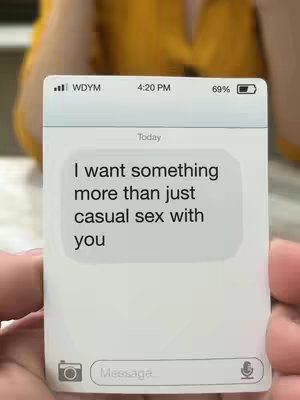 The image shows a smartphone screen displaying a text message, held by two hands. The screen shows a message bubble with the text "I want something more than just casual sex with you". The background includes a blurry yellow and tan color.