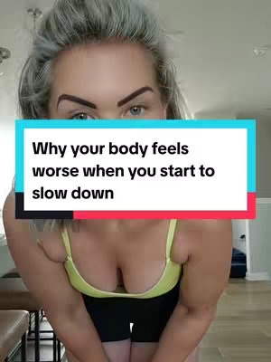A woman with gray hair and fair skin is centered in the frame, wearing a yellow sports bra and black shorts. A text overlay in a light blue box with red and black accents at the top reads, "Why your body feels worse when you start to slow down."