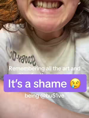 A close-up shot of a person's open mouth, showing teeth. The person appears to be about to speak. A purple banner with white text, "It's a shame 😢",  is superimposed on the image. The lower part of the person's shirt is visible, with a white and blue design.