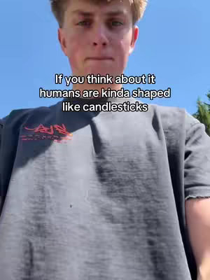 A young man in a grey t-shirt is centered in the frame with a light blue sky as the background. Text overlay is at the top in white indicating a humorous statement about the shape of humans and candlesticks. 