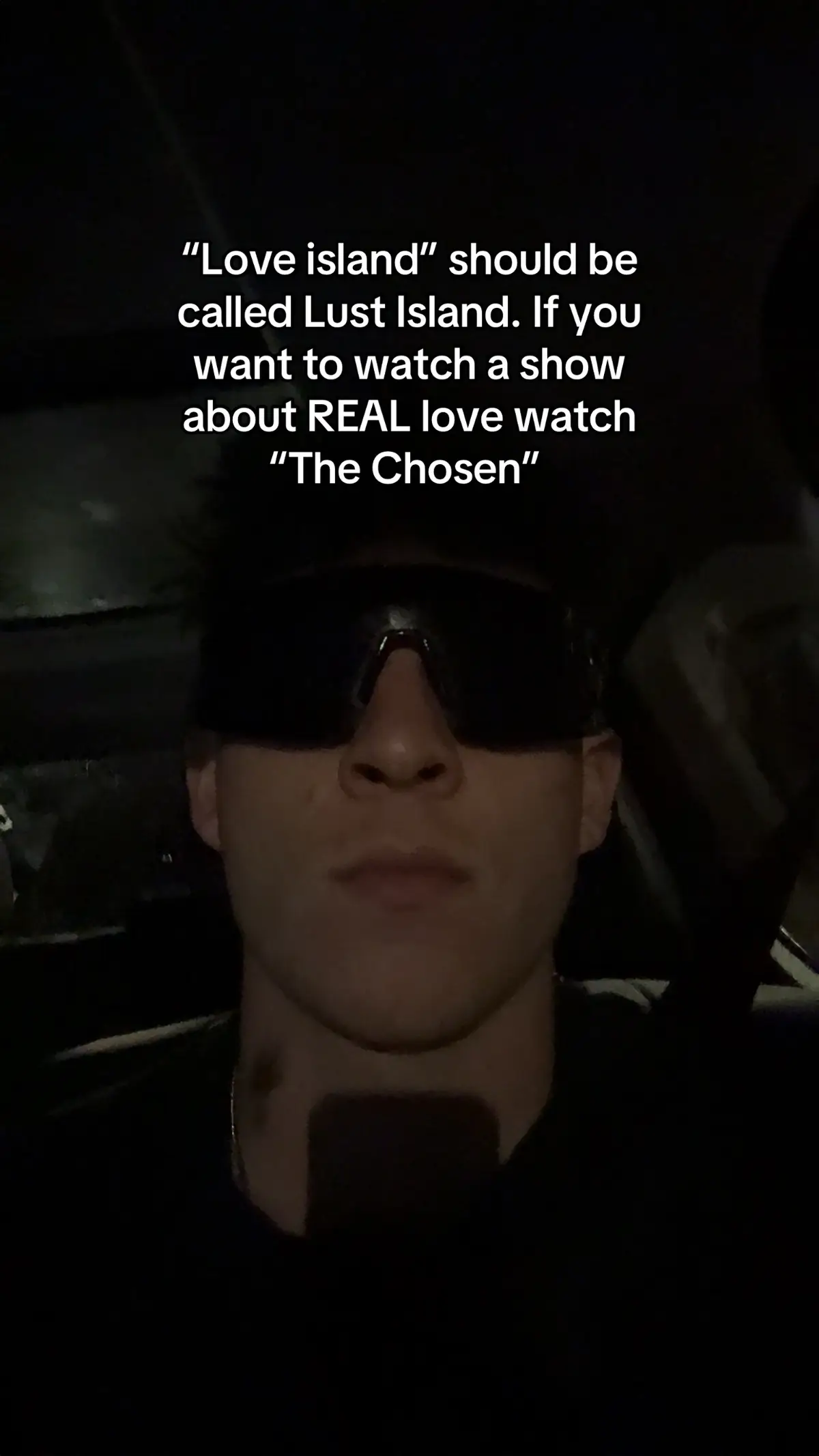 A selfie-style shot featuring a young man in the front seat of a car. He's wearing dark sunglasses and a black shirt, with text overlaid on the image.