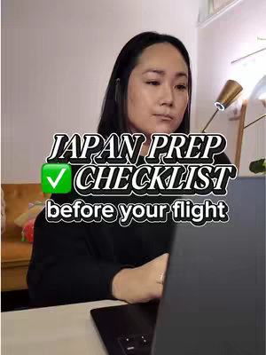 A woman is seated at a desk, facing the camera with a focused expression. A laptop is open in front of her. Text overlaid on the image reads "JAPAN PREP CHECKLIST before your flight" and a green checkmark logo.