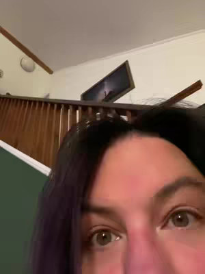The cover image is a close-up shot featuring the upper portion of a person's face, with the eyes prominently in view. The composition is dominated by the eyes, which have a light brown hue and are the central focus. The shot is angled upward, with the person's forehead and a portion of their dark hair visible above the eyes. The background includes a section of a wooden staircase with a picture hanging in the background.