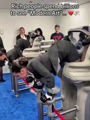 The image shows several people leaning over a series of white machines. The people, dressed in dark suits, are bent over with their backs to the viewer. The machines have a curved design and appear to have head rests. In the background, there are a few other people standing, including seemingly some observers. The overall impression is one of critique, with the hook text highlighting the artist's commentary.