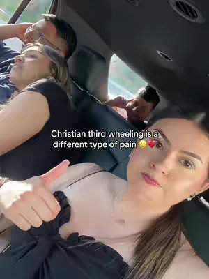 A selfie with a woman giving a thumbs-up in the front seat of a car. Behind her, two other people are visible in the back seat.