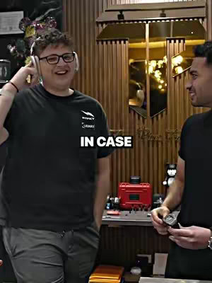 Two men are in what appears to be a store or shop setting. The man on the left is wearing headphones and a black t-shirt, with glasses, with the text overlayed: "IN CASE". The other man is on the right wearing a similar black t-shirt.