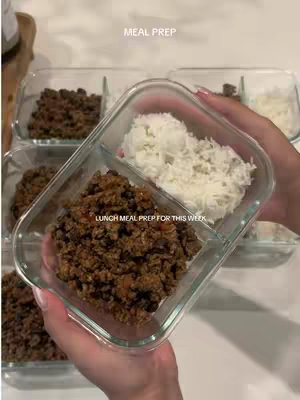 The cover image shows a close-up view of meal-prepped food in clear glass containers. The container in focus is divided into two sections: on the left, there's a portion of cooked ground beef, and to the right, a fluffy white rice. Other containers with identical meals are seen blurred in the background. The container is held by a person with well-manicured nails and a light skin tone, presented against a bright white background.