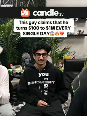 A man is centered in the image with text overlays. He wears glasses and a black hoodie with white text. Behind him is a blurred background of a room with plants and other objects. The overall composition is straightforward, with the focus on the man and the overlaid text.