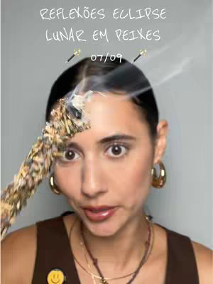 A person's face is centered in the frame, with a close-up view. A smoky incense stick is held near the forehead, and the person is looking at the camera with a slightly surprised expression. Text overlayed on top reads "REFLEXOES ECLIPSE LUNAR EM PEIXES" and "07/09". The background is plain.