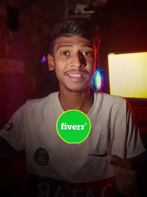A young man is smiling and looking at the camera, with the Fiverr logo overlaid on his chest. The background is dark, with some visible computer screens and some colorful neon lights. The man is wearing a white t-shirt with a logo on the left side.