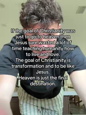 A selfie-style video cover image featuring a young man viewed from the chest up, slightly tilted down towards him. He is positioned in the center of the frame. He has short brown hair, and he wears a black t-shirt. The background is a blurred, neutral-toned interior. Text overlayed on the image presents an explanation of Christianity's core principle and Heaven as a reward.