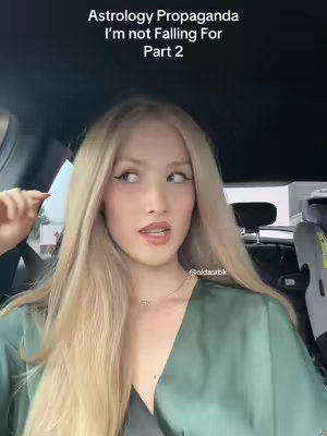 A woman with long blonde hair is in a car interior, with text overlayed on the top. She is looking away from the camera with a slight smile, wearing a green top and a necklace. The background shows a car dashboard and a glimpse of the outside world.