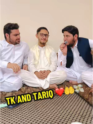 Three men are seated close together on a patterned rug, with a neutral background. The two men on the outer sides are smiling. The man in the middle is wearing glasses and appears to be looking at the camera. The man on the right is holding a microphone. A hook text is added at the bottom left, alongside heart, hand, and money bag emojis.