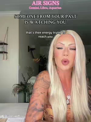 A woman with long blonde hair is centered in the frame, looking towards the camera. Above her head, there is text overlay. Below the text, more text is visible. The background seems to be a well-lit interior. The woman has tattoos on her arm and a necklace. The overall composition suggests a personal video.