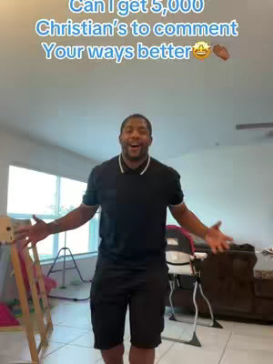 A man with a happy expression stands in a well-lit living room, arms outstretched, wearing a black polo shirt and shorts. Text overlay is in the top left corner. The room includes a high ceiling with recessed lighting, a wooden baby gate, and other furniture.