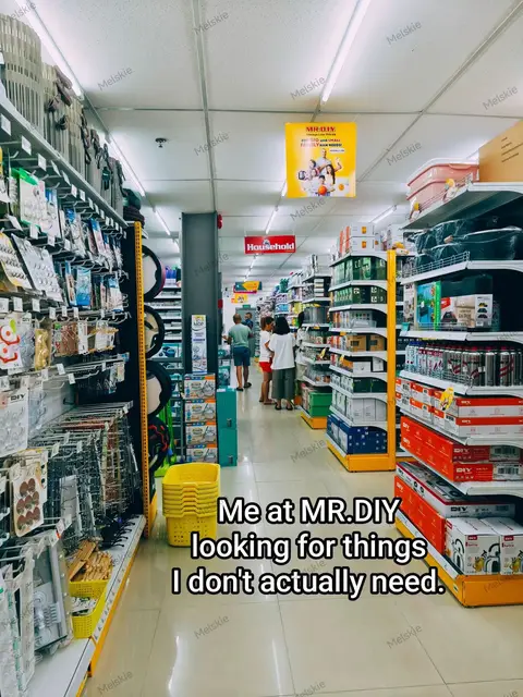A brightly lit interior shot of a Mr. DIY store with rows of shelves stocked with various merchandise. Text "Me at MR.DIY looking for things I don't actually need." is overlaid on the bottom. The scene depicts a typical shopping experience.