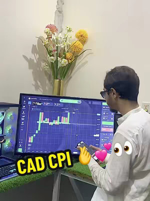A man wearing sunglasses and a white shirt is in front of a computer screen displaying a trading chart. A mobile phone is in his hand showing an app, with animated stickers like a pointing finger, hearts, and eyes overlaying the video.