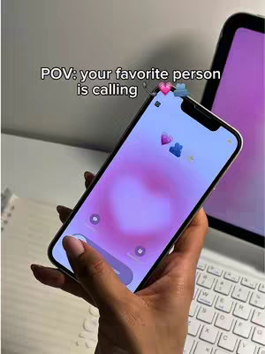 The cover image shows a closeup of a hand holding an iPhone. The phone screen displays a gradient pink and white background with a heart-shaped icon and a group of two figures icon. Overlayed at the top of the phone screen is text: POV: your favorite person is calling. In the background there is a laptop and a white surface.