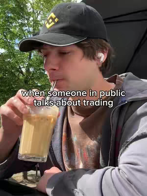 A young man wearing a black cap and a casual outfit is seated outdoors, sipping a drink with a straw. The background includes trees and sunlight.