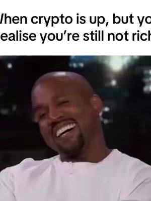 The image features a man with short hair, wearing a white shirt, laughing with his head tilted back. The background appears blurred, suggesting a studio or indoor setting. Text overlayed on the image reads, 'When crypto is up, but you realize you're still not rich'.