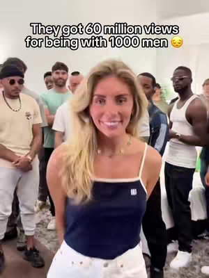 A woman in a blue top and white shorts stands smiling in front of a crowd of men. A text overlay at the top reveals the video's provocative claim.