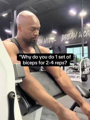 A man in a gym setting is seated on a machine. A text overlay is present on the image. The man has a bald head and is focused on the exercise.