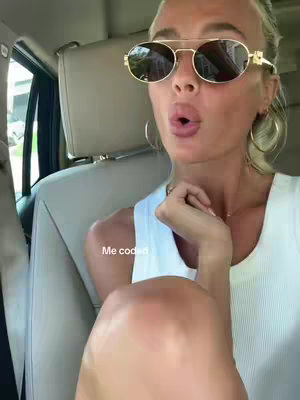 A woman wearing sunglasses is sitting in the front seat of a car. She has blonde hair and is gazing at the camera with her mouth slightly open. The text 'Me coded' is overlaid on the image.
