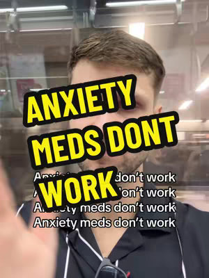 A selfie-style video features a man with short brown hair, set against a blurred indoor background with overhead lights. A yellow and black overlay covers his face and a portion of his chest, displaying the text "ANXIETY MEDS DONT WORK" in bold, capital letters. The word "WORK" is especially prominent due to its size.