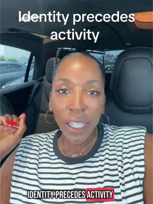 A woman is filming herself inside a car. The text overlay at the top reads "Identity precedes activity" and The bottom text overlay also reads "IDENTITY PRECEDES ACTIVITY". The woman has dark hair, hoop earrings, and a striped top. Behind her is the interior of the car and a blurred view of the outside.