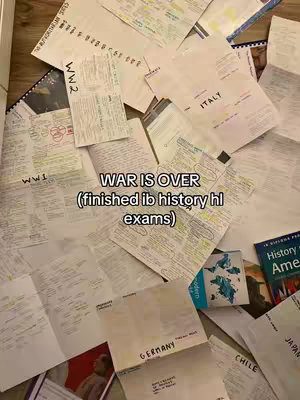 A top-down image shows a scattered arrangement of papers, notes, and study materials spread across a surface, likely a wooden floor. The papers vary in size and shape, some with handwritten notes and diagrams. Text overlays read 'WAR IS OVER', suggesting the relief of finishing exams. The color palette is dominated by white paper and ink.