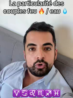 A man with dark hair and a beard is in the center of the frame, looking directly at the camera with an open mouth as if speaking. The background is a light gray sofa. Text overlays the top of the image in white. Below the man, a purple bar displays astrological symbols.